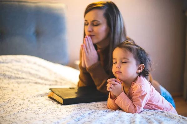 depositphotos_547613810-stock-photo-mother-her-daughter-reading-bible imagem com uma mãe orando com seu filho pequeno ao entardecer, sentados juntos ao ar livre, com uma Bíblia aberta no colo. Expressa intimidade, ensino e fé.