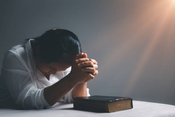 istockphoto-1473104259-612x612 Mulher orando sentada ao pôr do sol, com expressão de cansaço e esperança