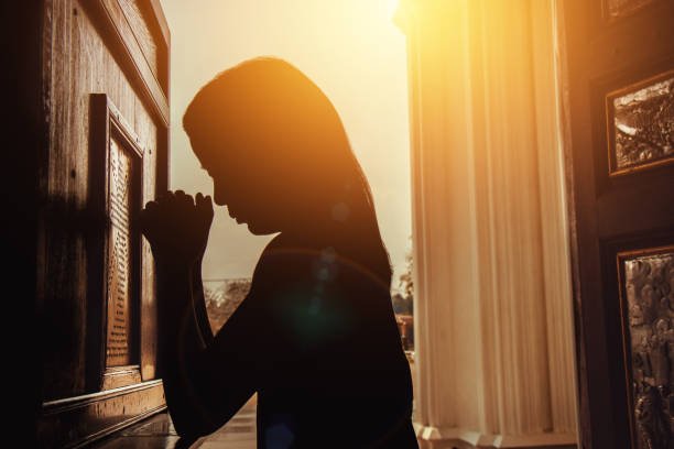 silhouette of woman kneeling and praying in modern church at sunset time mulher orando ajoelhada com luz entrando pela janela
