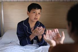 download (1) mãe e filho de mãos dadas, orando antes de dormir, à luz suave de um abajur, transmitindo paz, fé e amor.