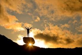 download (19) pessoa de braços erguidos diante de uma montanha iluminada pelo nascer do sol, simbolizando fé e superação.