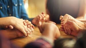 download (3) família reunida de mãos dadas em oração ao redor da mesa, com luz suave ao entardecer.”