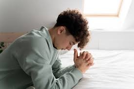 download (6) pessoa orando de joelhos em um quarto simples, luz suave entrando pela janela, simbolizando fé e entrega.