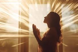 download Mãos erguidas em oração diante de uma janela iluminada pelo amanhecer.